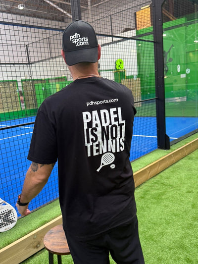 Person wearing a black t-shirt with 'Padel is not Tennis' text in an indoor sports facility.